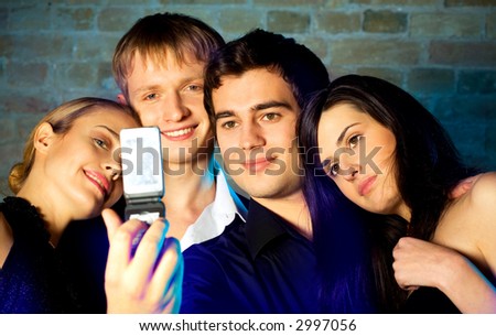 Young embracing smiling people taking photograph by cellphone and posing at celebration or night party