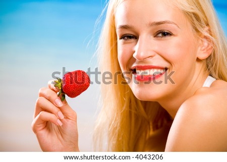 Young beautiful tanned happy sexy smiling blond woman with strawberry on sea beach
