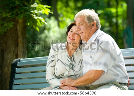 Happy elderly couple listening music in headset together, outdoors