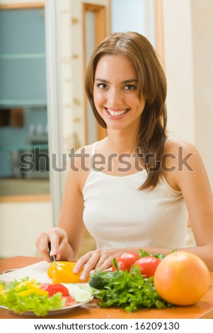 Young happy woman making salad at domestic kitchen