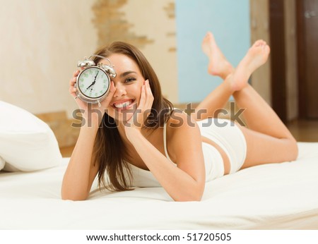 Young woman with alarmclock on the bed at the morning