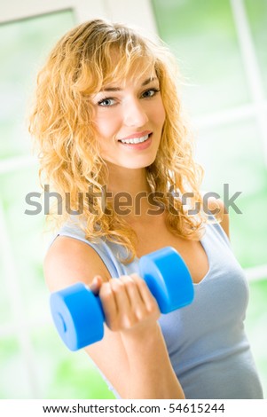 Young happy woman exercising with dumbbell at home