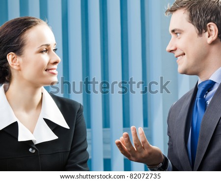 Two happy smiling young businesspeople, or businessman and client, working at office