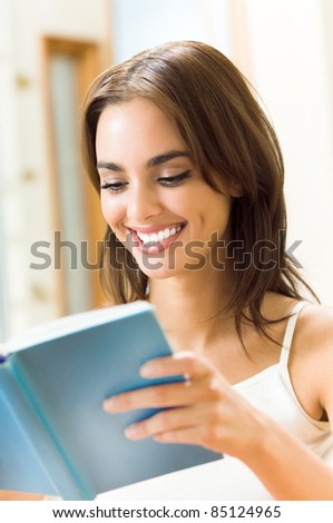 Portrait of young happy smiling beautiful woman reading a book or textbook at home