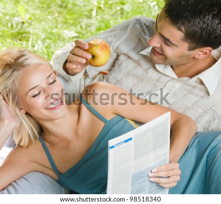 Young happy smiling cheerful couple reading together newspaper, outdoors