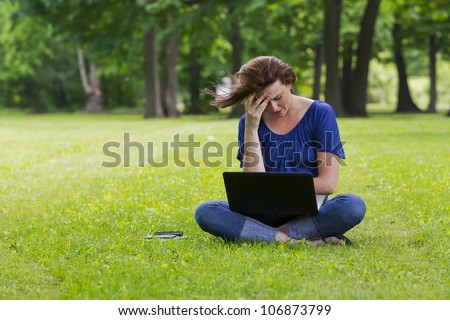 A beautiful brunette model working on a computer and talking on a mobile phone in an outdoor environment