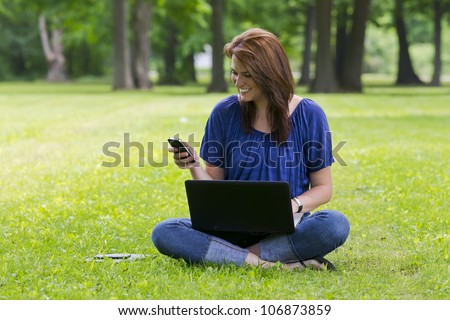 A beautiful brunette model working on a computer and talking on a mobile phone in an outdoor environment