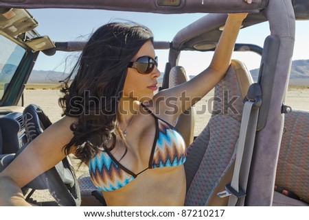 A brunette bikini model posing in a desert environment in an open top vehicle