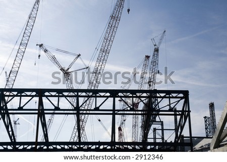 New industrial building construction site. Silhouettes of cranes and building frame against blue sky background