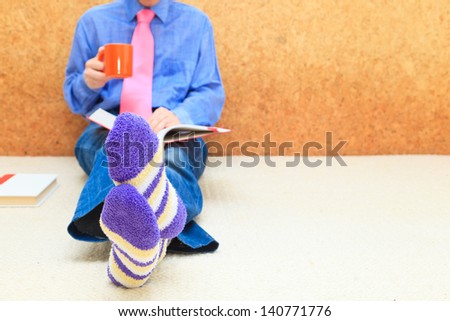 Home study. Businessman reading book with cup of coffee at home, close up on male foots in socks.