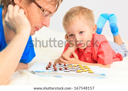 father and son playing checkers, early education and family concept