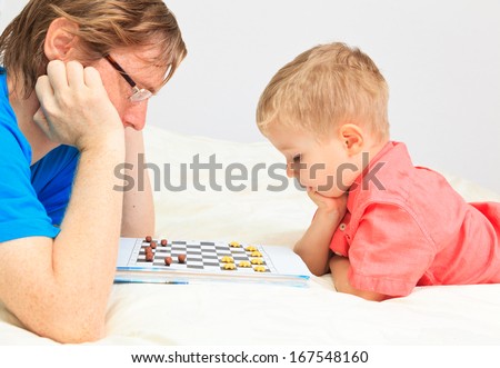 father and son playing checkers, early education and family concept