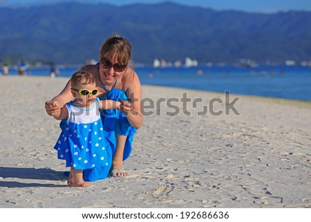 mother teaching her daughter to walk her first steps on tropical beach