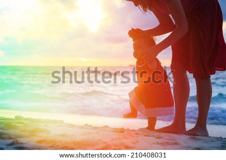 mother and little daughter walking on sand beach at sunset