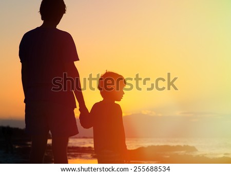 father and son holding hands at sunset sea