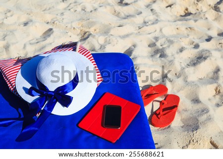 hat, bag, touch pad, mobile phone and flip flops on a tropical beach