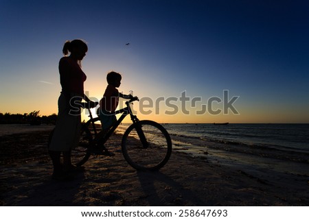 Silhouette of mother and son biking at sunset sea