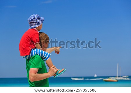 father and little son on shoulders pointing at the sea on summer beach