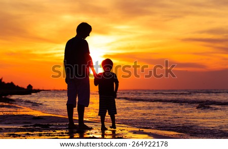 silhouettes of father and son holding hands at sunset sea