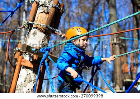 little boy climbing in adventure activity park with helmet and safety equipment