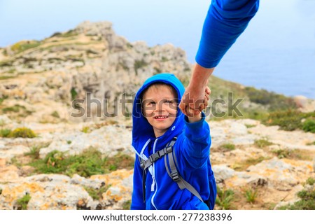 Helping hand- little boy helped by parent on hiking in mountains