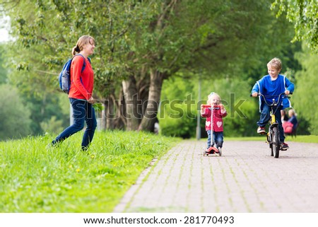 happy mother with two kids on scooter and bike in the park, family sport