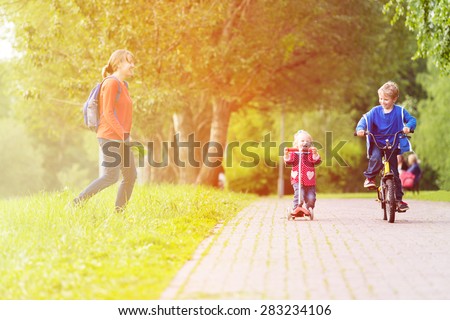 happy mother with two kids on scooter and bike in the park, family sport