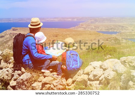 father with two kids looking at map in mountains, family travel