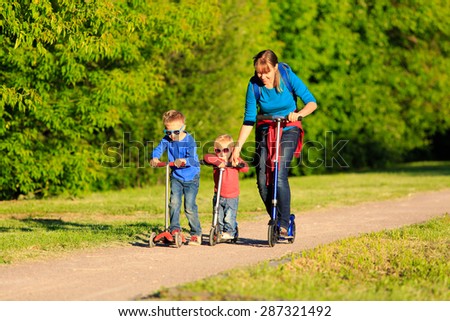 mother with kids riding scooters in summer, family sport