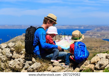 father with two kids looking at map in mountains, family travel