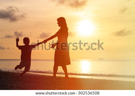 silhouettes of mother and son having fun on sunset beach