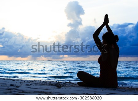 young woman meditation on sunset tropical beach