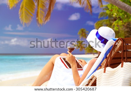 woman drinking wine and looking at touch pad on tropical beach