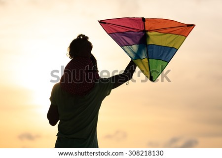 father and little daughter having fun flying kite at sunset