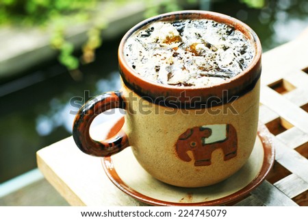 iced coffee americano in ceramic cup with elephant cartoon mosaic cup on wood table