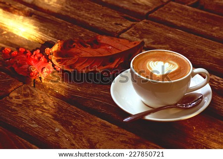 Fall or Autumn morning Cup of latte or cappuccino coffee setting on wooden table with fall leaves  with pastel mood vintage retro filter effect
