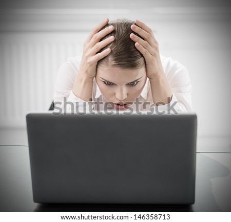 Young woman with computer worried about work done. Portrait of businesswoman with scared expression sitting in the office.