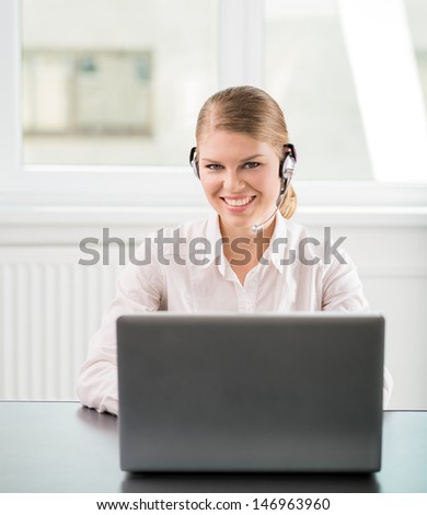 Joyful attractive headphones woman with laptop at work. Happy professional support operator working in the office.