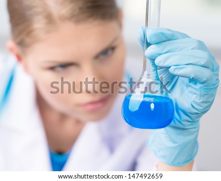 Young female scientist testing liquid for chemical experiment in laboratory.