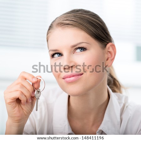 Close-up of young house buyer with a key dreaming of new property for her family. Attractive Caucasian woman model in real estate agent\'s office.