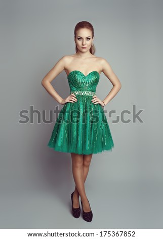 Pretty woman in luxury green dress wearing high heels. Young attractive Caucasian blond model in beautiful evening clothes posing in studio.