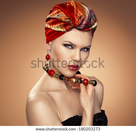 Pretty fashion girl in turban wearing red earrings, touching her necklace. Beautiful Caucasian blue eyed model with ethnic make-up and hairstyle.