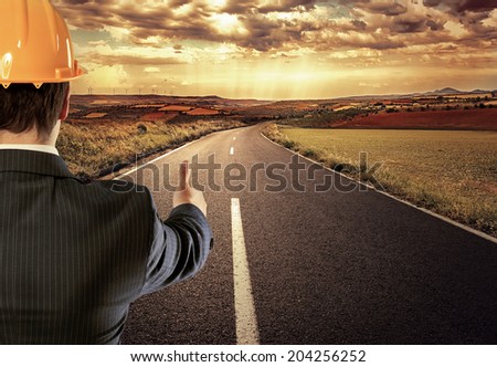 Male engineer on straight asphalt road showing thumb up as sign of success.