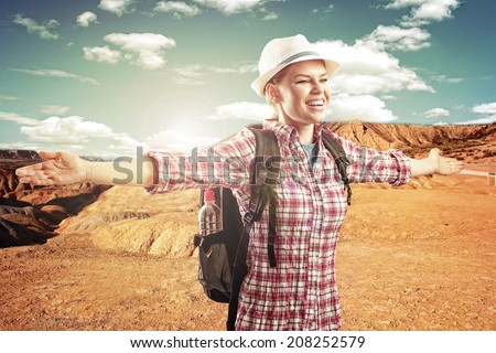 Happy smiling female traveler with backpack in the desert. Young sporty woman discovering beautiful desert landscape.