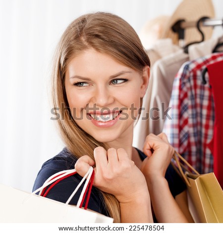 Cheerful shopping girl with gift bags standing in retail store looking in mirror.