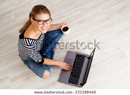 Portrait of young smiling female searching internet for interior design of her new house. Beautiful Caucasian girl sitting on the floor of empty room.