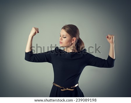 Powerful and strong business woman concept. Young female in dress looking at her muscled arms posing in studio.