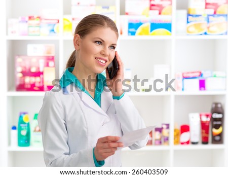 Portrait of female pharmacist consulting customer on phone holding recipe. Young woman medical assistant in pharmacy.