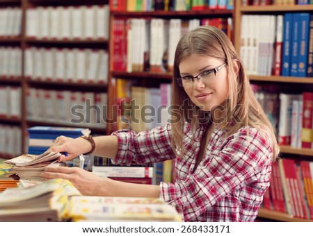 Young female small business owner arranging magazines and press in the retail bookstore.