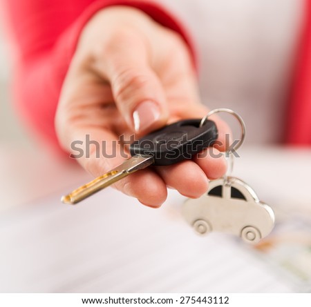 Closeup of female hand giving car key to buyer in automotive dealer\'s office. Auto rent, sale and inspection concept. Shallow depth of field.
